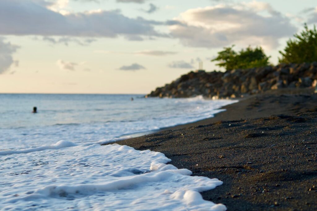 Calm ocean waves on a black sand beach in Guadeloupe with a serene sunset backdrop.